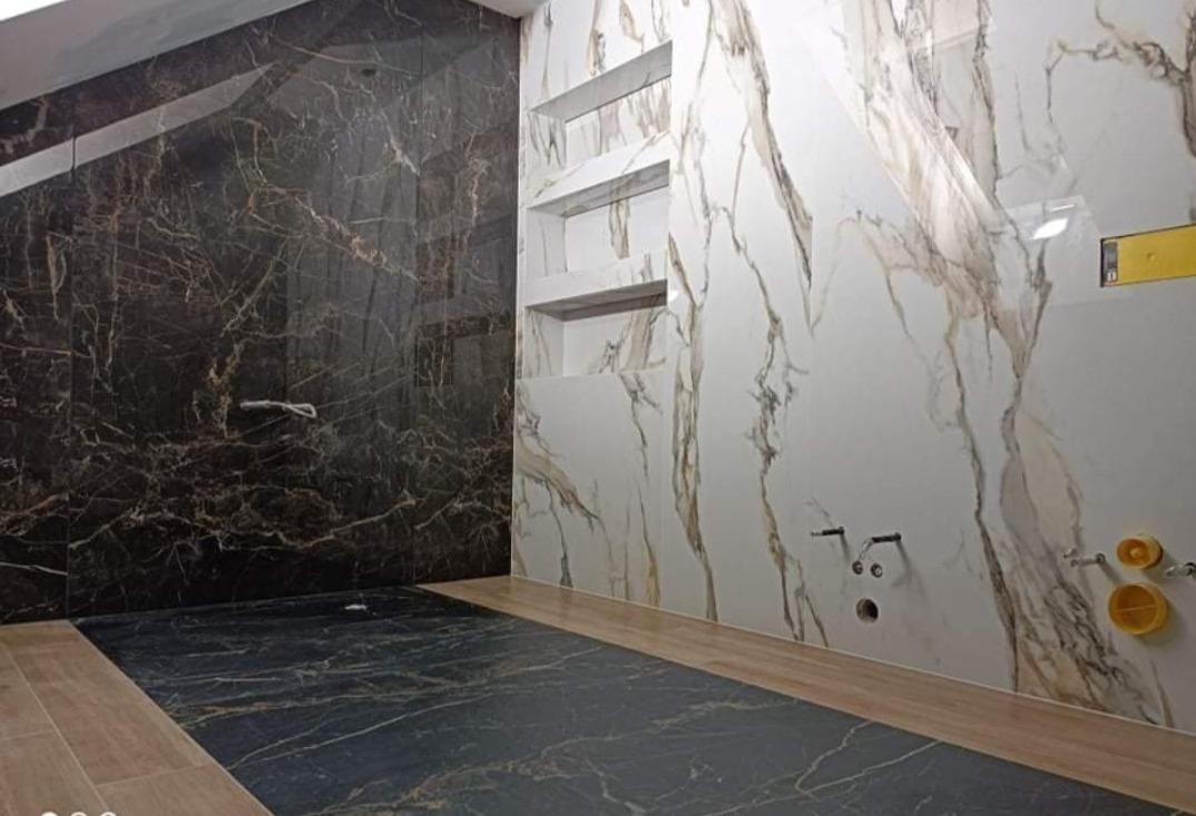 Wykończona łazienka z czarnymi i białymi marmurkowymi płytkami, wnęki w ścianie, przygotowane instalacje wodno-kanalizacyjne.