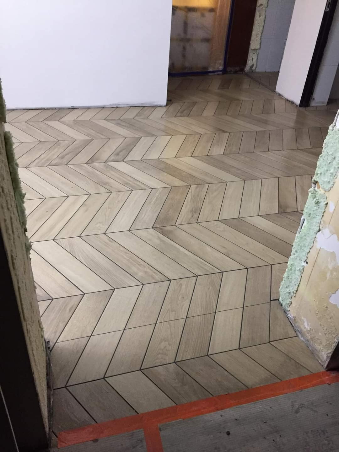 Ułożona w jodełkę jasna glazura imitująca drewno na podłodze, widoczne niedokończone wykończenia ścian.