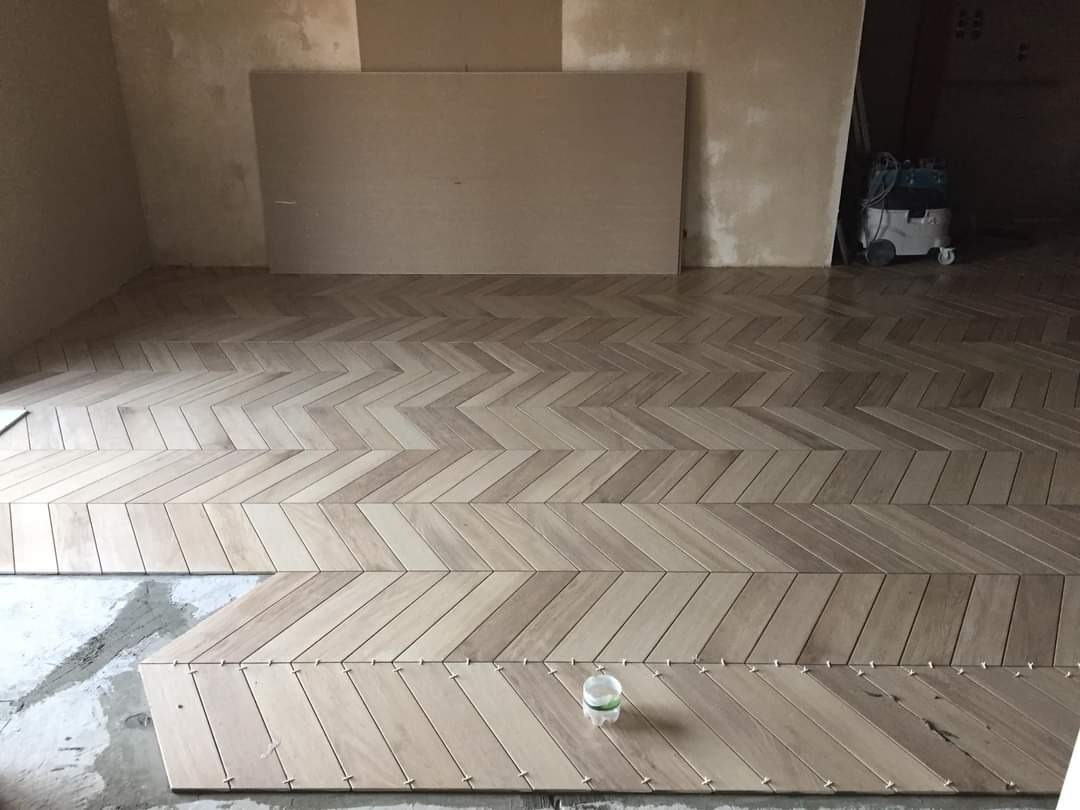 Układanie parkietu w jodełkę, widoczny fragment podłogi w trakcie prac, z plastikową butelką i odkurzaczem przemysłowym w tle.