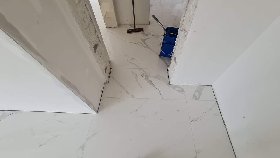 Biała marmurowa podłoga z widocznym mopem i wiadrem, ściany w trakcie wykończenia, surowy stan