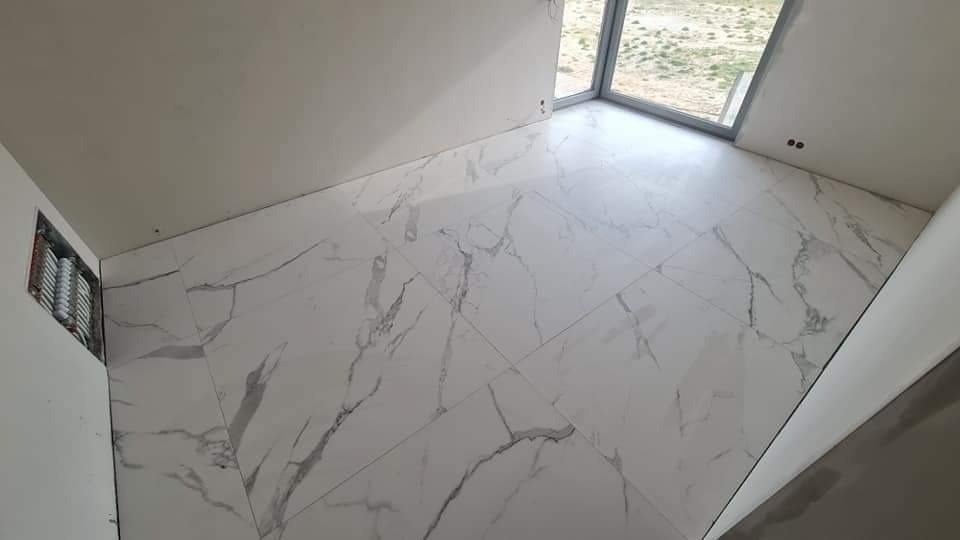 Wykończona podłoga w pomieszczeniu z białych, marmurkowych płytek, widok z góry na okno z widokiem na zewnątrz.