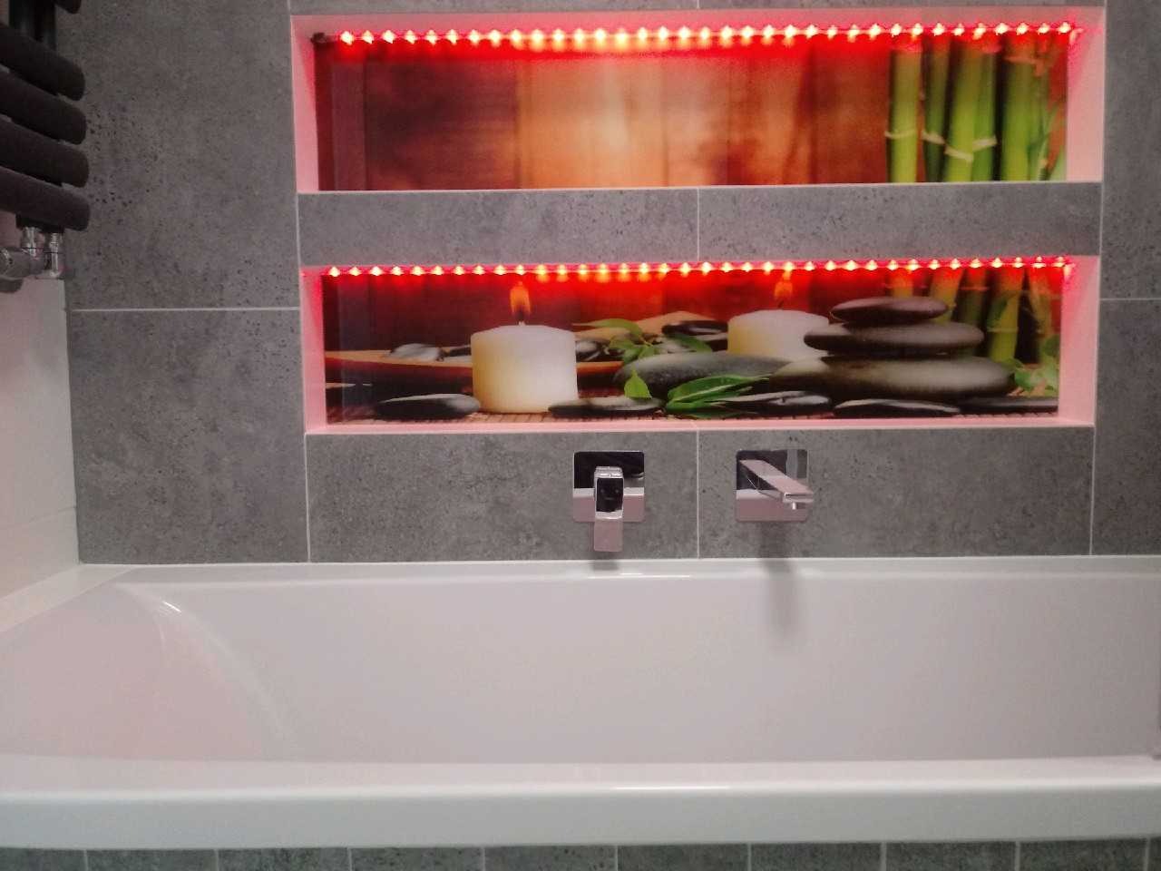 Nowoczesna łazienka z wanną i wnękami podświetlonymi czerwonymi diodami LED, w których umieszczono dekoracje zen: bambus, kamienie i świece.