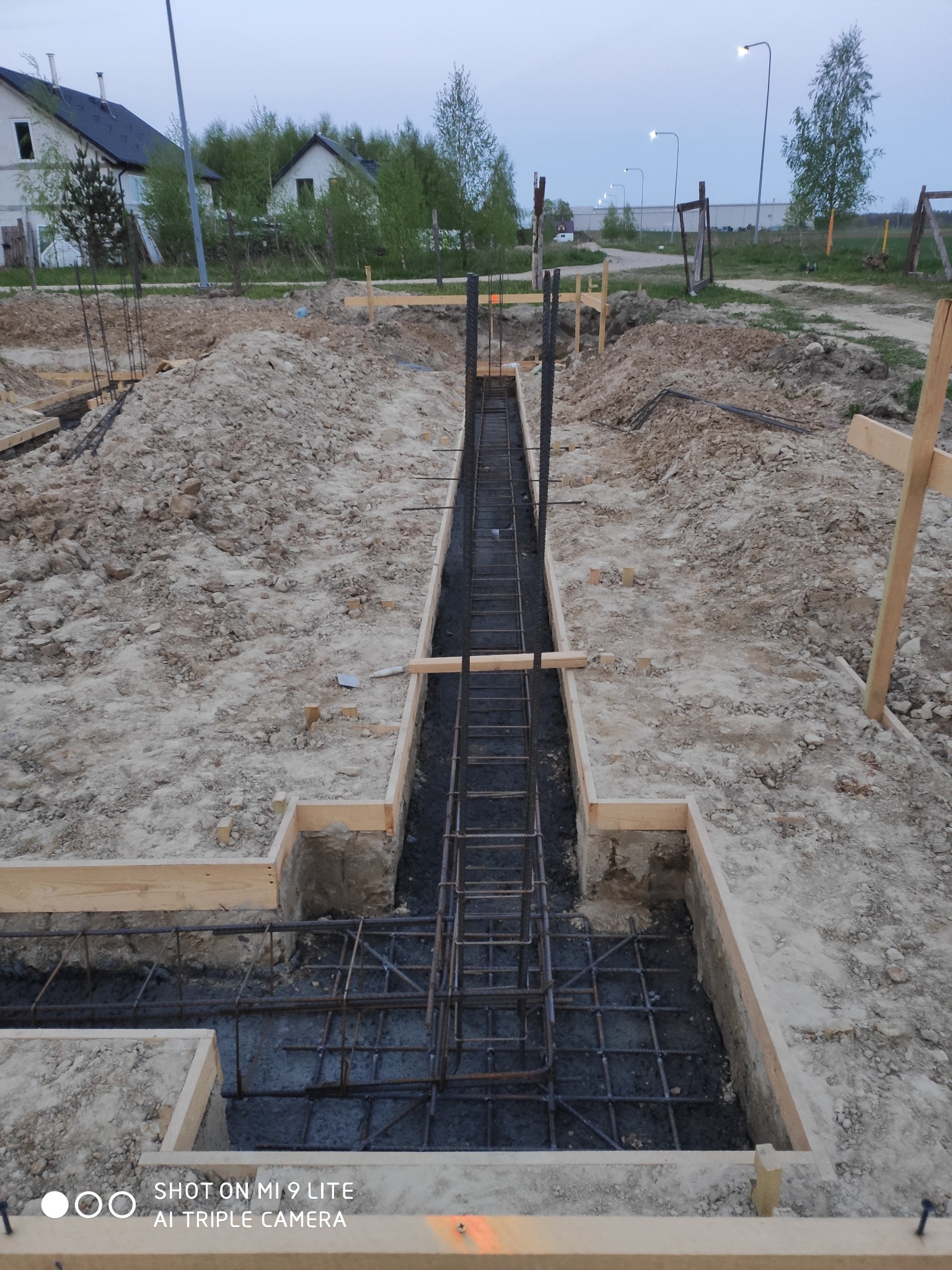 Wykop fundamentów z drewnianym szalunkiem i zbrojeniem stalowym, widok z góry na plac budowy w pochmurny dzień.