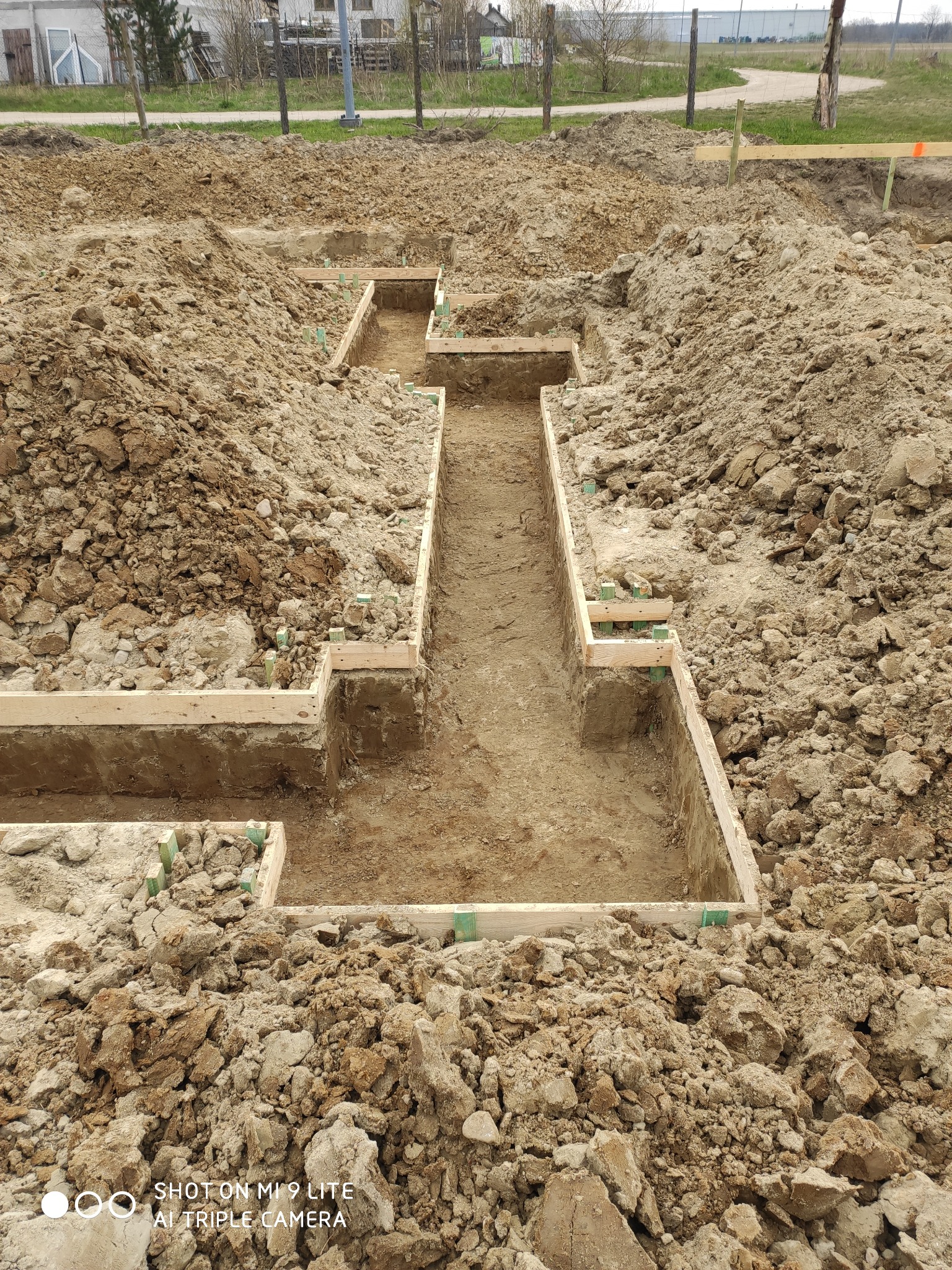 Wykonane wykopy pod fundamenty domu z drewnianym szalunkiem, widoczne pryzmy ziemi.