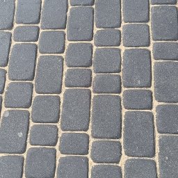 Simon Wash - Ułożona, szara kostka brukowa o nieregularnych kształtach, wypełniona piaskiem. Widok z góry, oświetlenie dzienne.