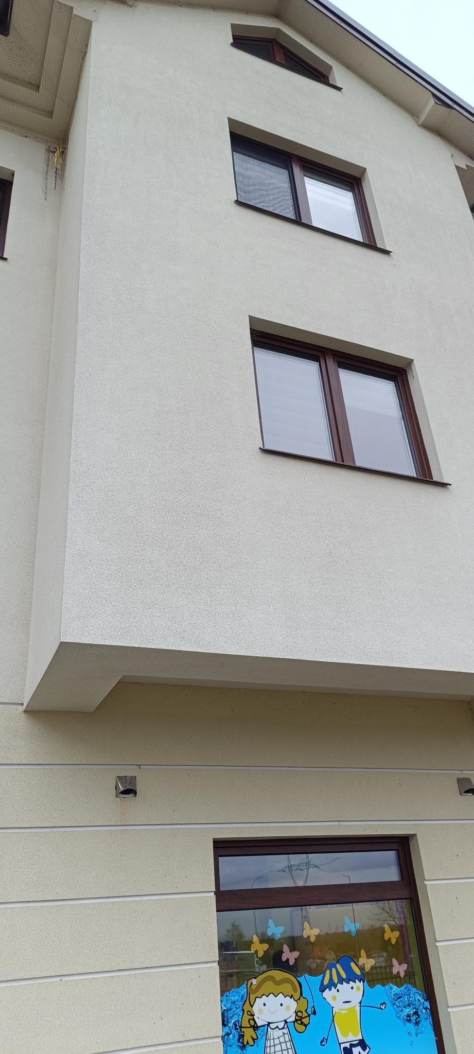 Fragment elewacji budynku z oknami i dekoracją okienną w postaci rysunków dziecięcych.