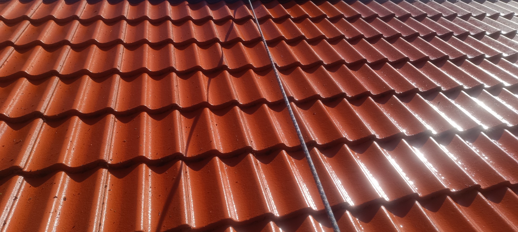Czerwona dachówka ceramiczna, połowa dachu umyta, widoczna różnica w czystości i kolorze, lina na dachu, perspektywa z dołu.
