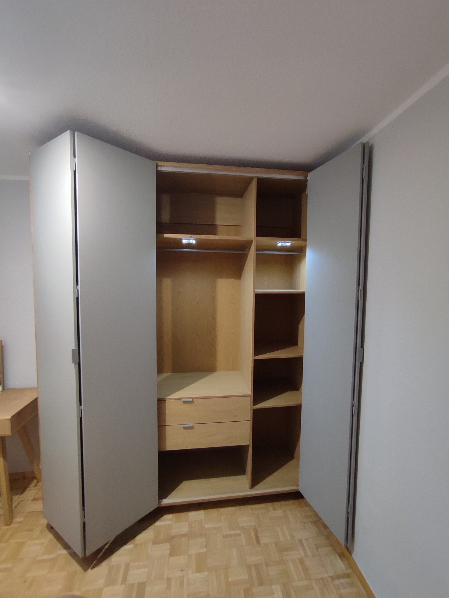 Otwarta szafa na wymiar z drewnianymi półkami i szufladami, oświetleniem LED wewnątrz, z szarymi drzwiami na tle parkietu.