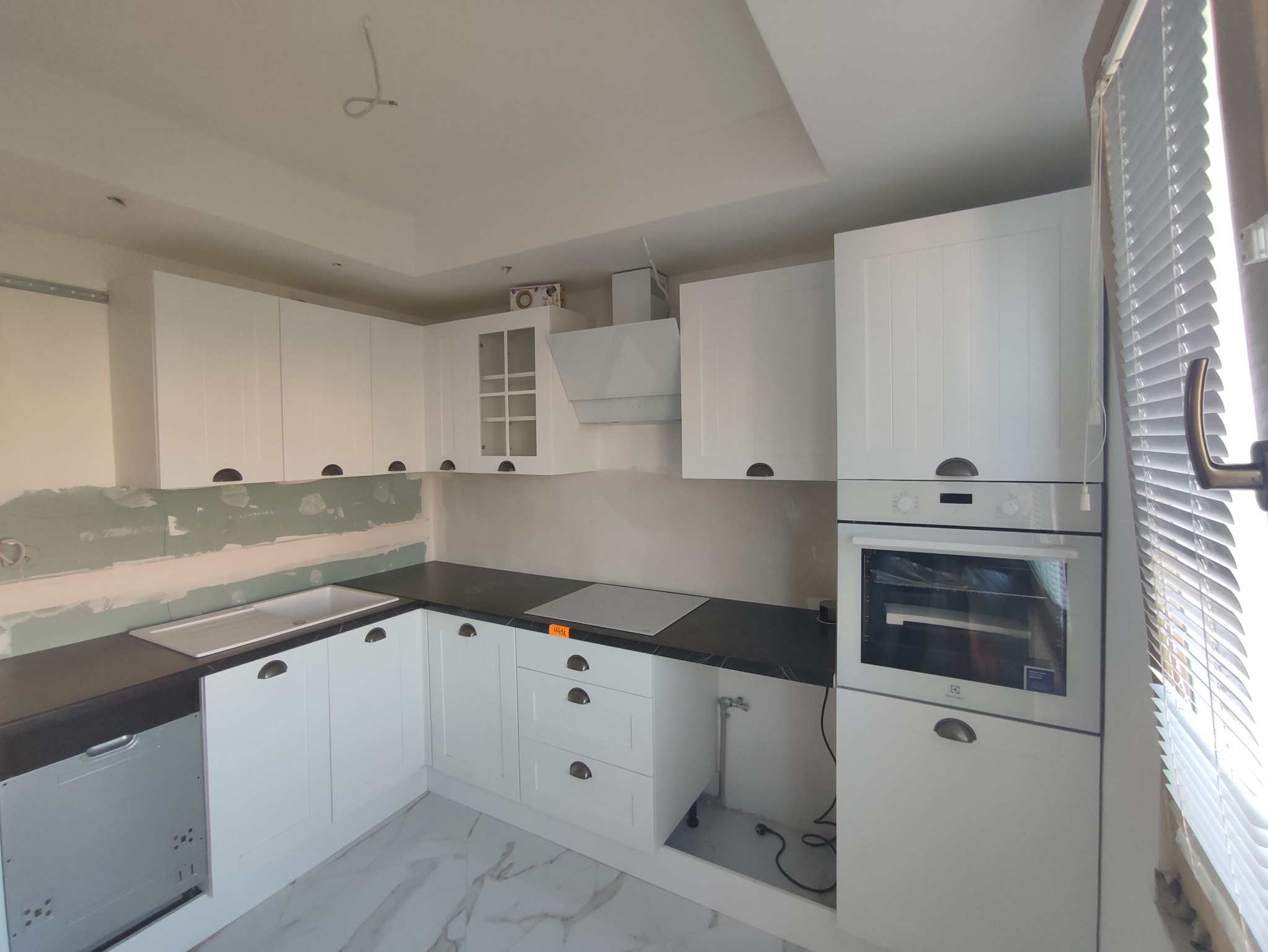 Wnętrze kuchni w trakcie montażu: białe szafki z ciemnym blatem, widoczne niedokończone ściany i instalacje.