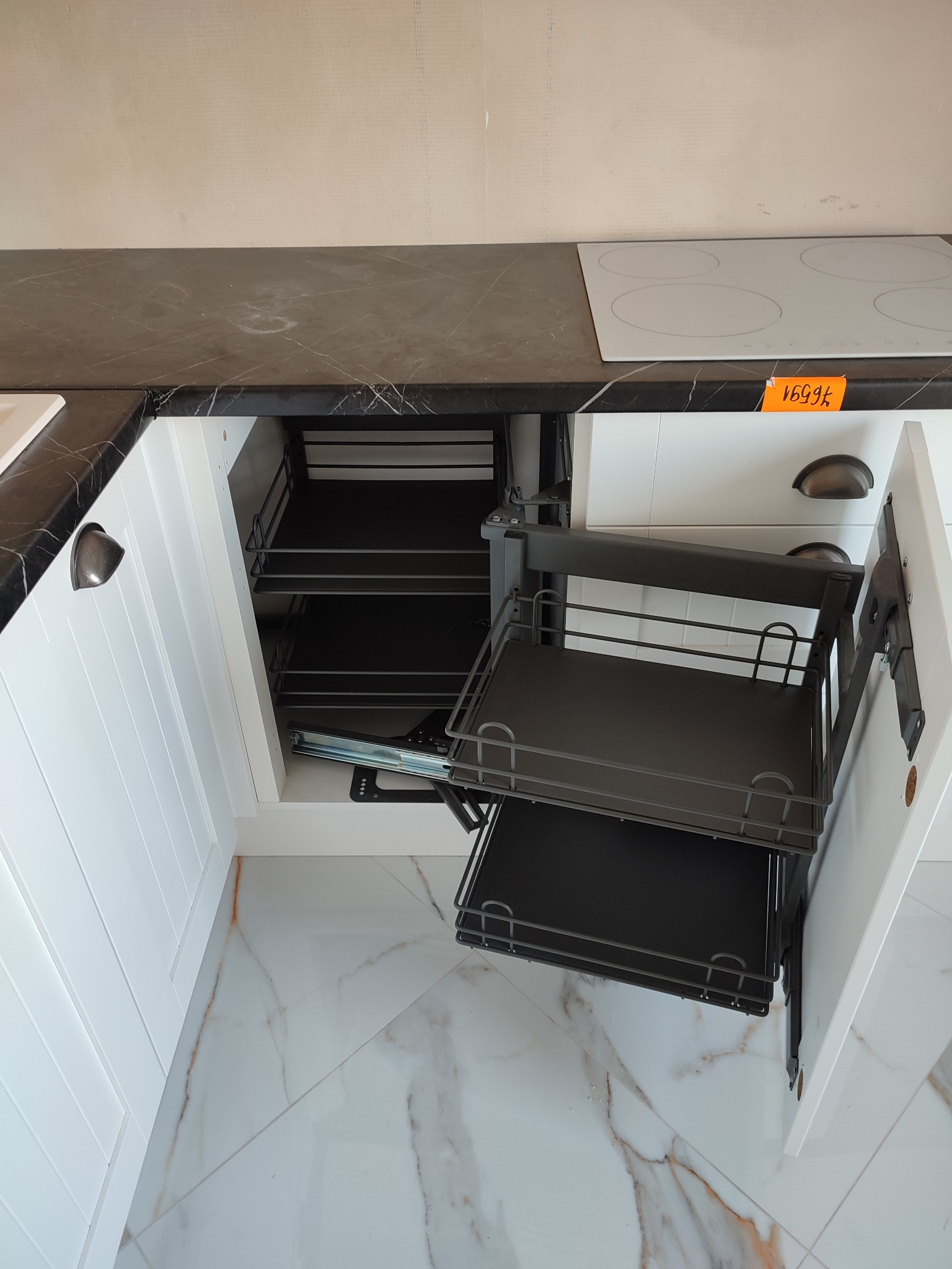 Wysuwany, metalowy kosz cargo zamontowany w białej szafce kuchennej z blatem imitującym marmur, widok z góry na podłogę z płytek imitujących marmur.