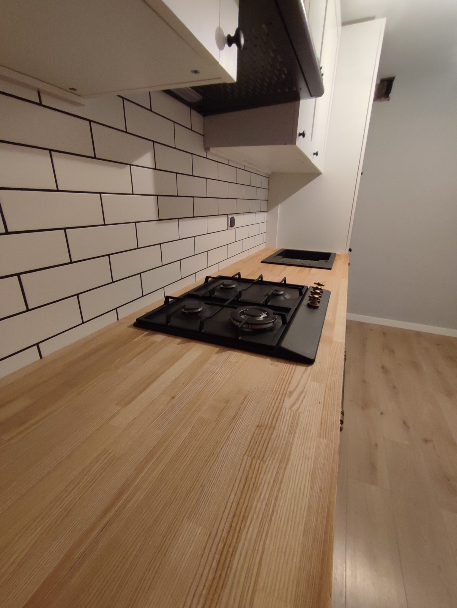 Nowoczesna kuchnia: drewniany blat, czarna płyta gazowa i białe kafelki w stylu metro z czarną fugą.
