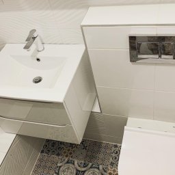 ADREM Adrian Świerzbin Remonty Łazienki Wykończenia - Nowoczesna, biała umywalka z szafką i chromowaną baterią w łazience z dekoracyjnymi płytkami podłogowymi i falistymi płytkami ściennymi.