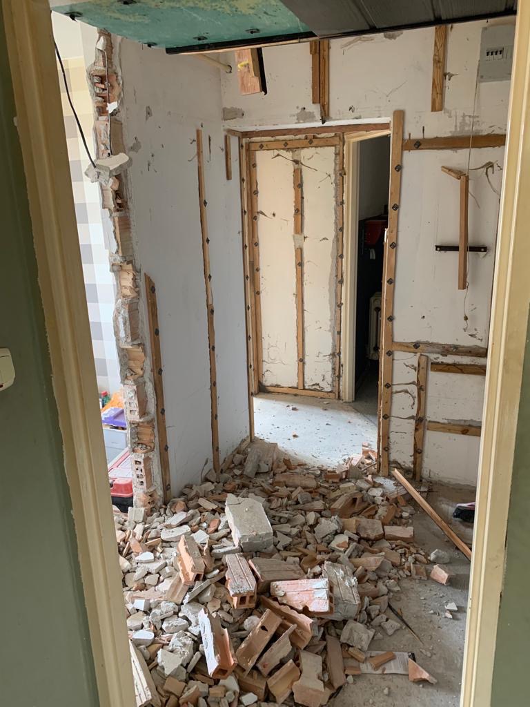 Wnętrze w trakcie rozbiórki: fragment ściany z odsłoniętą konstrukcją drewnianą i stertą gruzu ceglanego na podłodze, widoczne pozostałości instalacji elektrycznej.