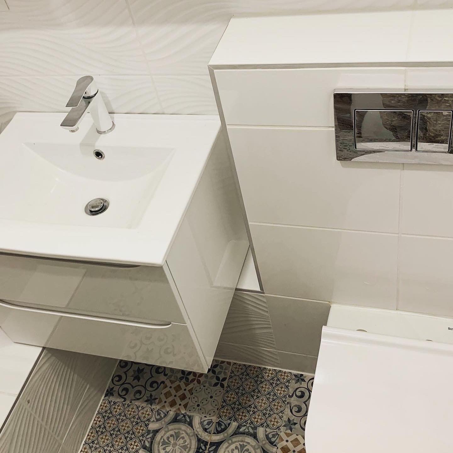 Nowoczesna, biała umywalka z szafką i chromowaną baterią w łazience z dekoracyjnymi płytkami podłogowymi i falistymi płytkami ściennymi.