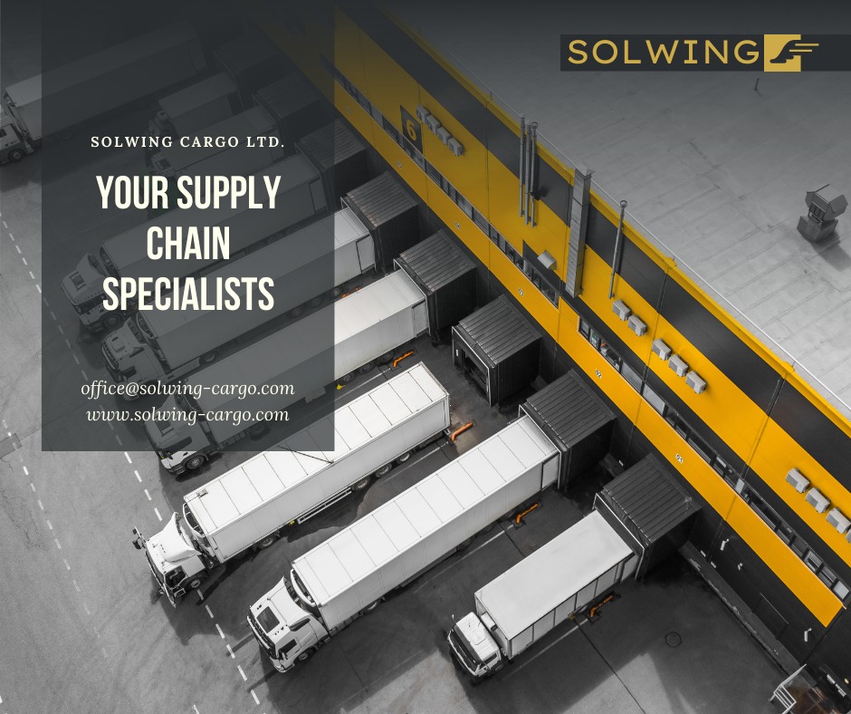 Widok z góry na zaparkowane ciężarówki z naczepami przy magazynie z żółto-czarnymi pasami, logo Solwing Cargo LTD.