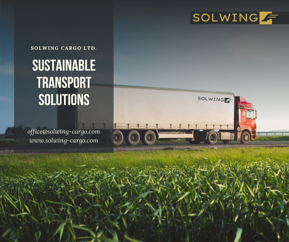 Czerwona ciężarówka z białą naczepą firmy Solwing Cargo LTD. jadąca po asfalcie na tle zielonego pola, z logo firmy na naczepie i w prawym górnym rogu.