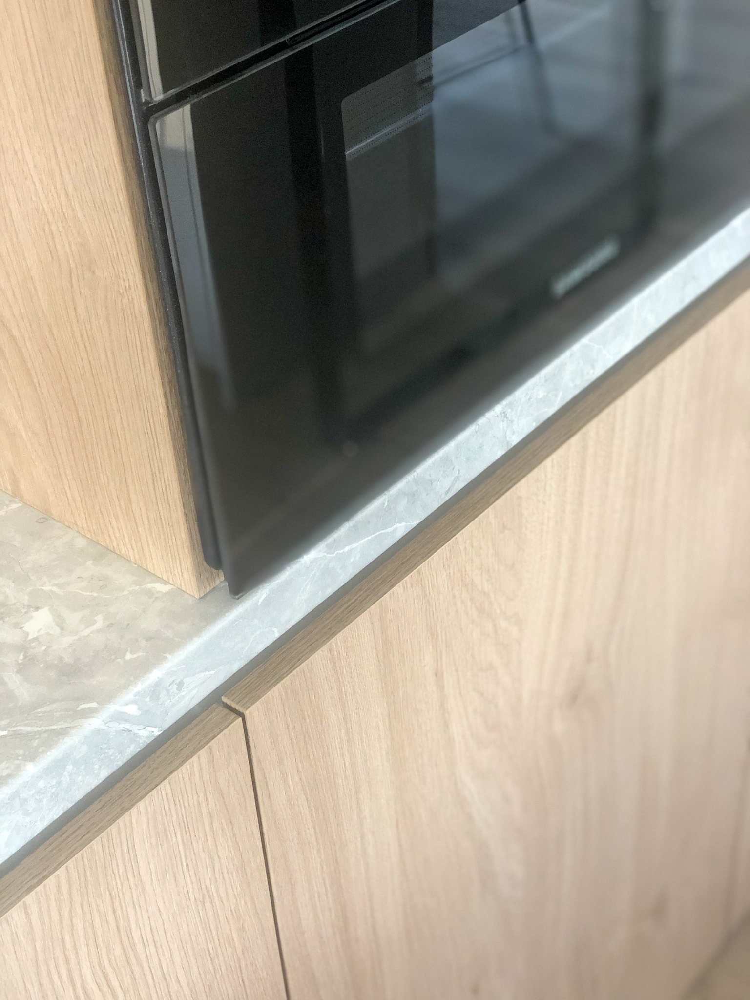 Fragment zabudowy kuchennej: drewniane fronty szafek, marmurowy blat i wbudowany piekarnik z czarnym frontem.