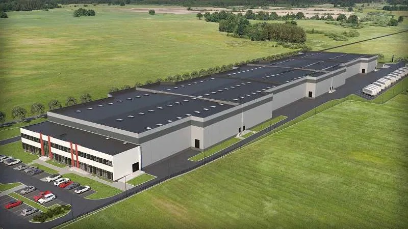 Wizualizacja zewnętrzna rozległego, nowoczesnego magazynu z parkingiem dla samochodów osobowych i przestrzenią dla kontenerów, otoczonego rozległymi, zielonymi terenami trawiastymi.