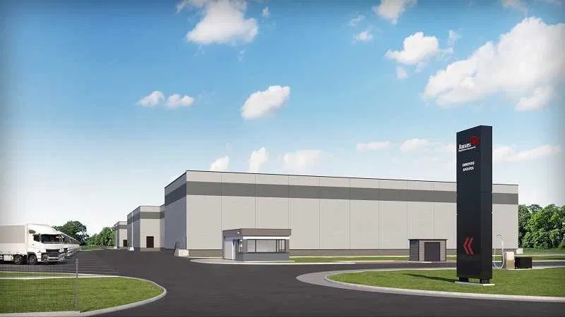 Nowoczesny kompleks magazynowy z zaparkowaną ciężarówką, widoczny budynek ochrony i wysoki pylon z logo firmy.