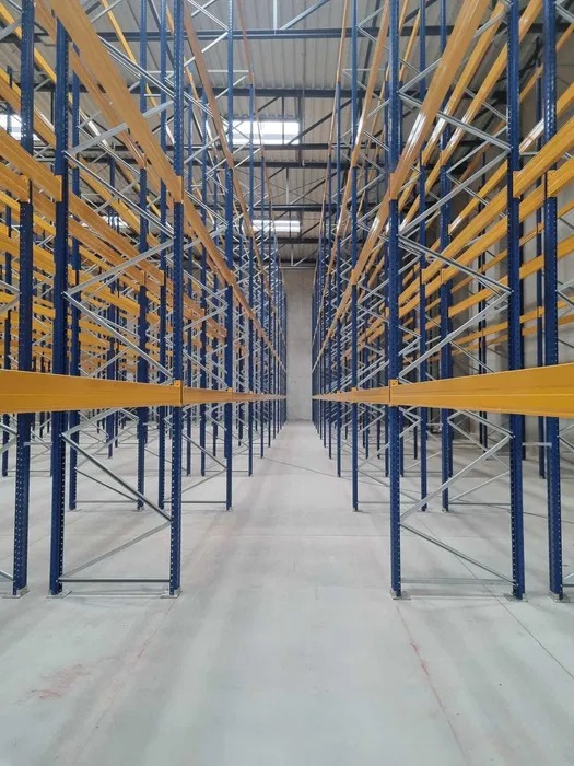 Puste, niebiesko-żółte regały magazynowe w hali w Skwierzynie, widok z perspektywy podłogi w głąb korytarza między regałami.