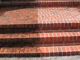 Częściowo wyczyszczone ceglane schody zewnętrzne; po lewej stronie widoczny ciemny nalot, po prawej czysta, czerwona cegła.