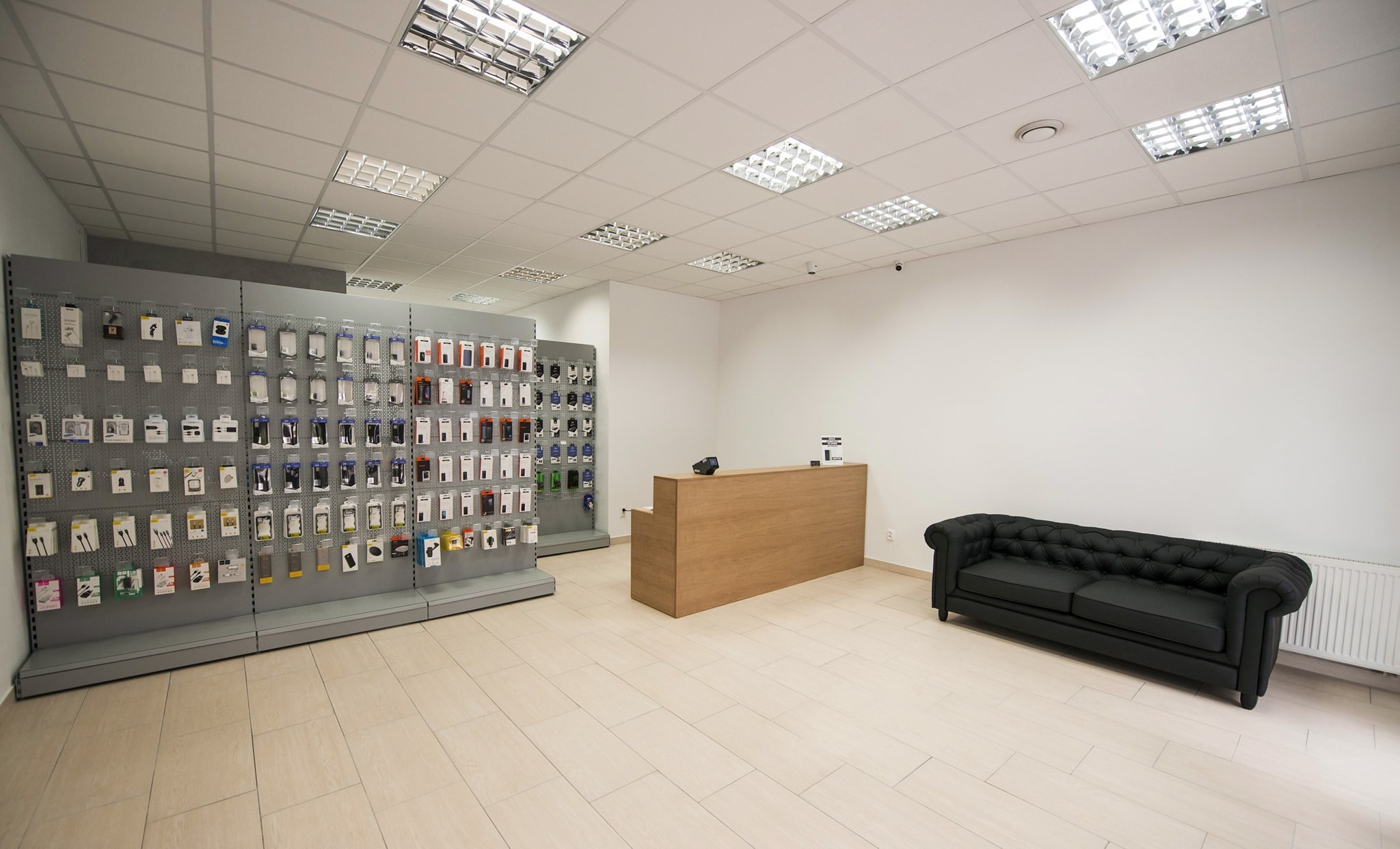 Wnętrze sklepu z akcesoriami do telefonów: ekspozycja słuchawek i ładowarek na ścianie, drewniana lada i czarna sofa w stylu chesterfield.