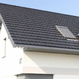 Nowoczesny dom z ciemnoszarą dachówką ceramiczną i oknem dachowym z żaluzjami, widok na fragment elewacji z rynnami i numerem budynku.