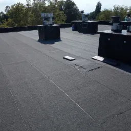 Płaski dach pokryty papą termozgrzewalną z kominkami wentylacyjnymi, widoczne łączenia papy i detale obróbek.