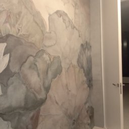 FRBIW Damian Lumer - Ściana w pokoju z ręcznie malowanym wzorem dużych, abstrakcyjnych kwiatów w odcieniach szarości i beżu, widoczna biała ościeżnica i drzwi.