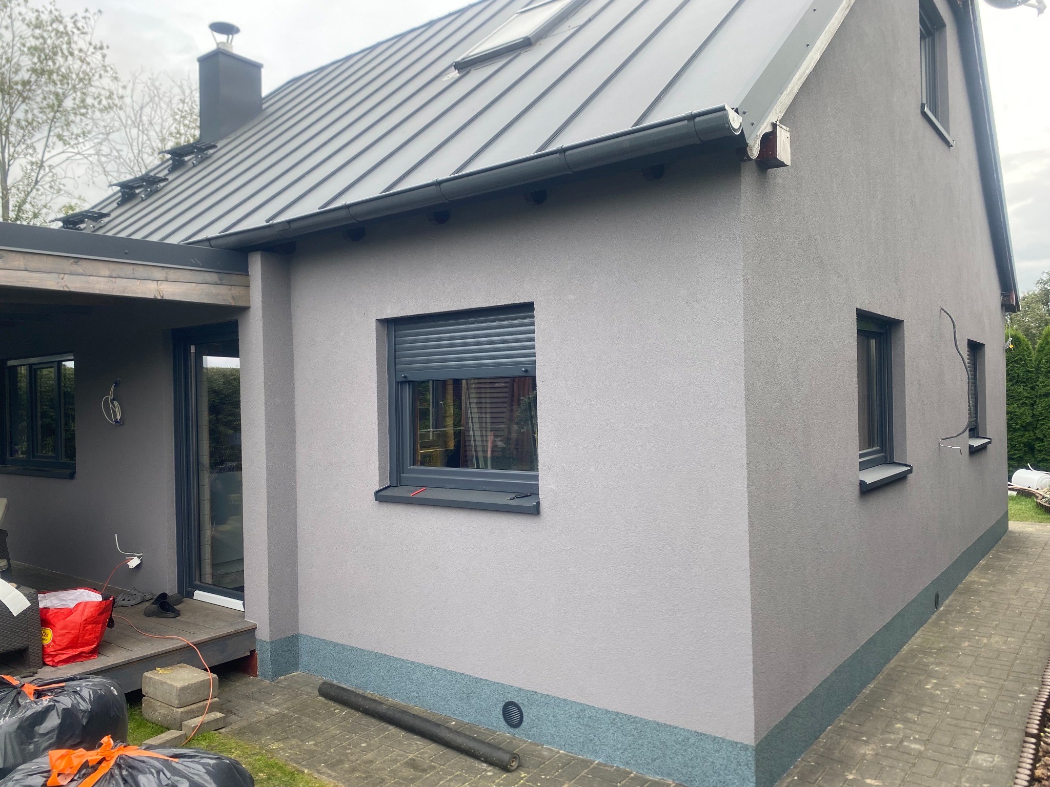 Szary dom jednorodzinny z metalowym dachem i elewacją w odcieniach szarości, widok z boku, z elementami wykończeniowymi w podobnej tonacji.