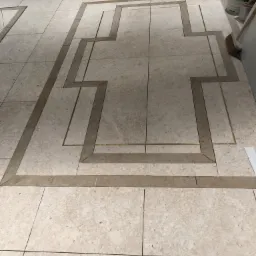 Ułożona podłoga z płytek w beżowych odcieniach z dekoracyjnym wzorem geometrycznym z płytek w innym odcieniu, widoczne narzędzia i materiały budowlane.