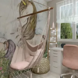 Pokój dziecięcy z motywem jednorożców na ścianie, hamak fotel zawieszony na drewnianej belce, biurko z lampką i krzesłem w kolorze pudrowego różu, drabinka z lampkami, jasne kolory.