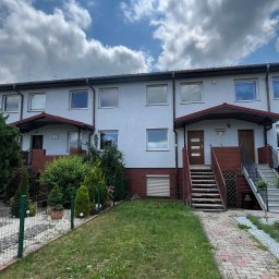 ALIGATOR Alicja Gatlik - Szereg domów z szarą elewacją, brązowymi rynnami i czerwonymi ceglanymi elementami, widok z poziomu trawnika w pochmurny dzień.