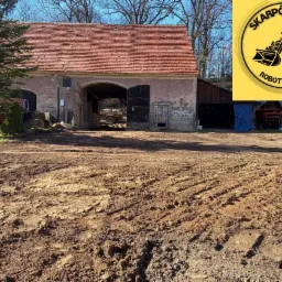 Ujęcie terenu po pracach ziemnych z widocznym budynkiem gospodarczym z czerwonym dachem w tle oraz logo firmy w prawym górnym rogu.