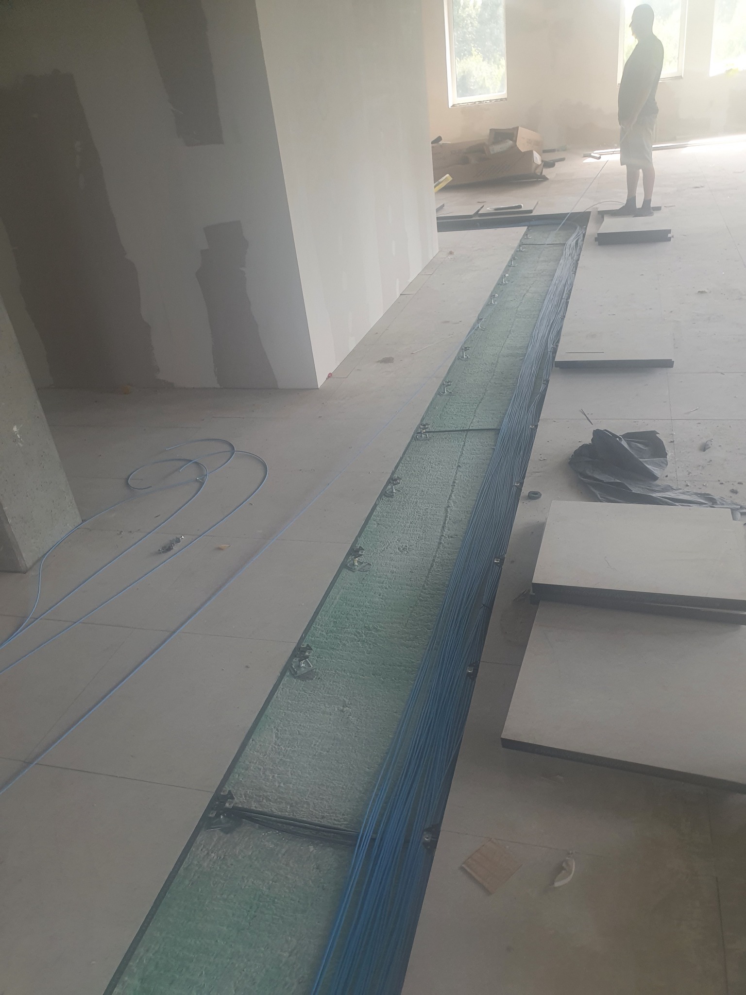 Wnętrze w trakcie remontu, widoczne kable elektryczne ułożone w korycie pod podłogą, przygotowane do zalania wylewką, oraz ułożone płyty podłogowe.