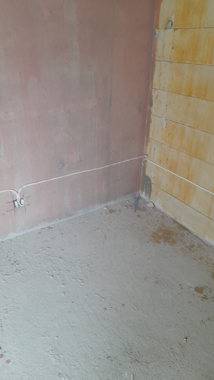 Surowy stan wnętrza: ściany z widocznymi przewodami elektrycznymi, surowy beton na podłodze, ściana z bloków z betonu komórkowego.