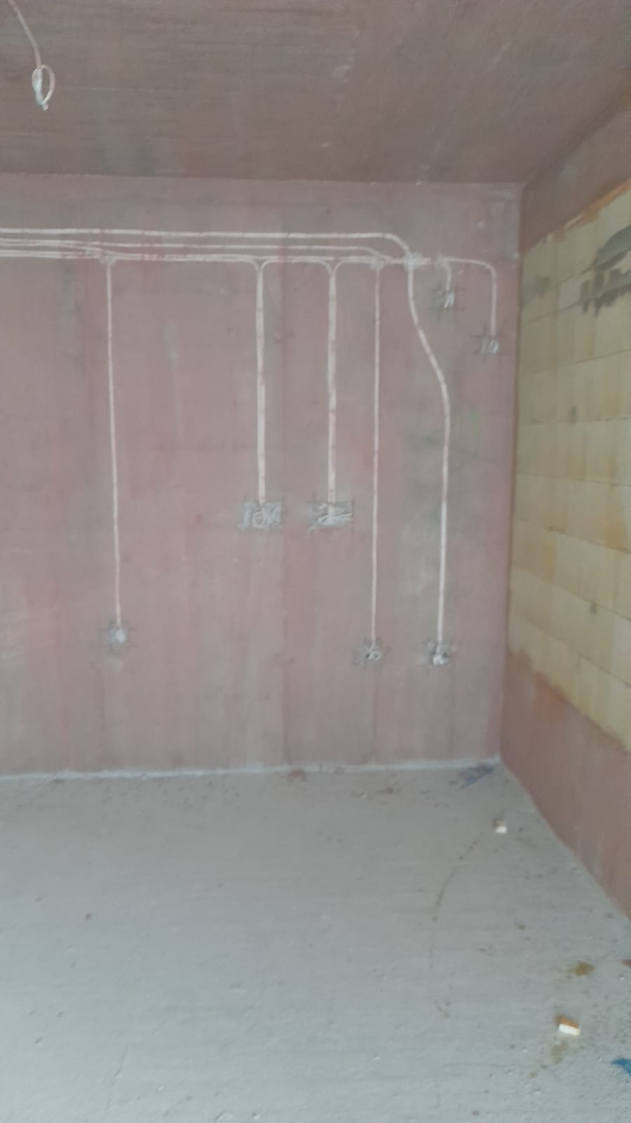 Ściana w trakcie remontu z rozprowadzonymi przewodami elektrycznymi podtynkowo, widoczne puszki instalacyjne i fragment ściany z żółtymi płytkami.