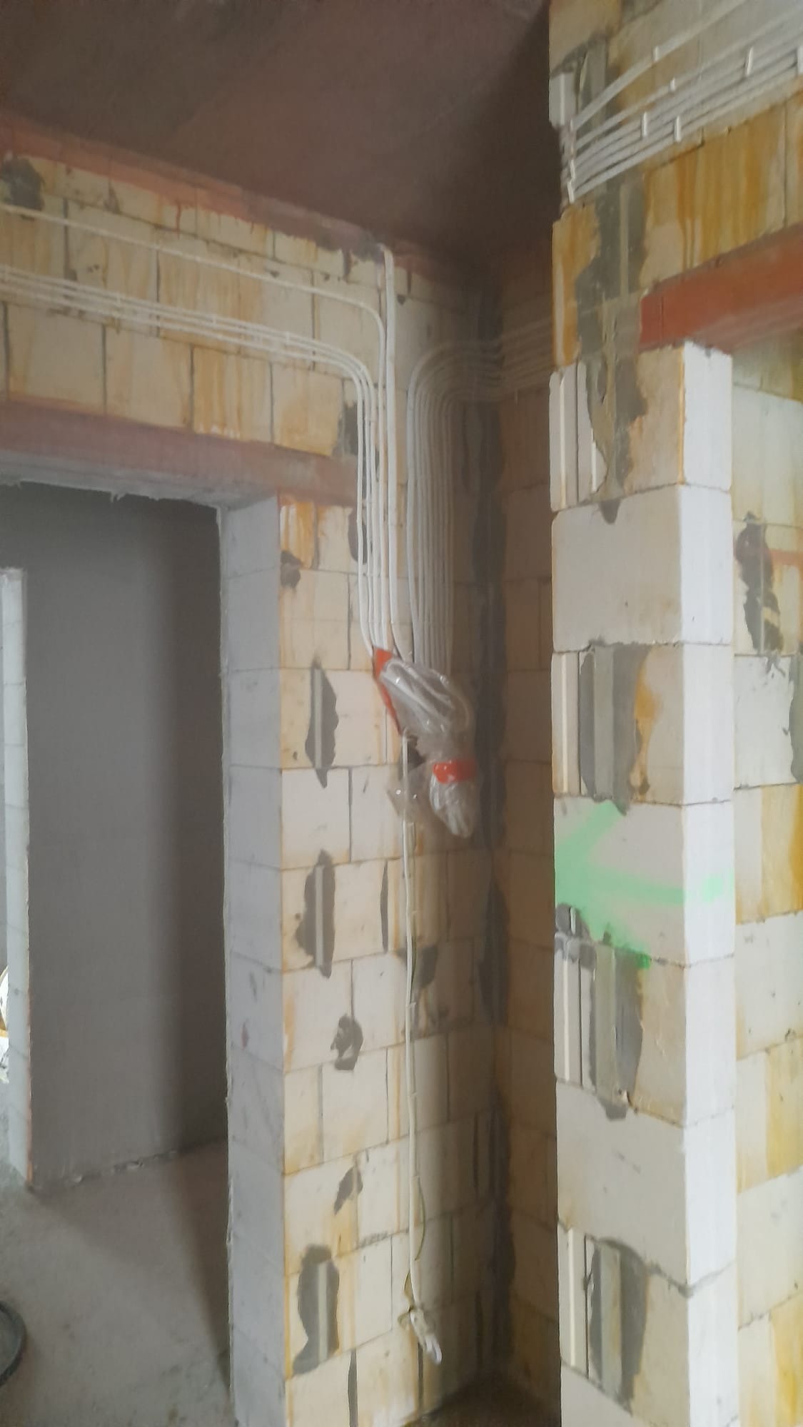 Instalacja elektryczna w trakcie montażu: przewody prowadzone po ścianach z bloczków, zabezpieczone folią na łączeniu, widoczne ślady zaprawy.