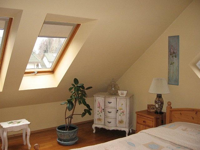 Pokój na poddaszu z oknami dachowymi, ściany pomalowane na kremowo, drewniana podłoga, meble w stylu vintage i dekoracje.