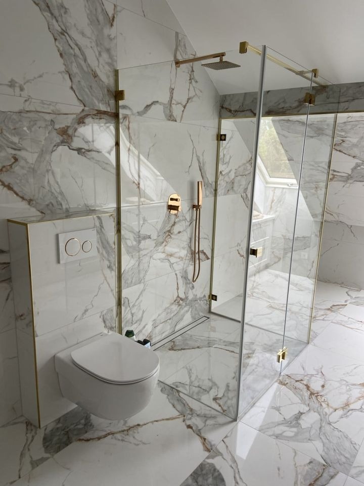 Nowoczesna łazienka z kabiną prysznicową typu walk-in, wykończona marmurem z złotymi akcentami, wisząca toaleta z podtynkową spłuczką.