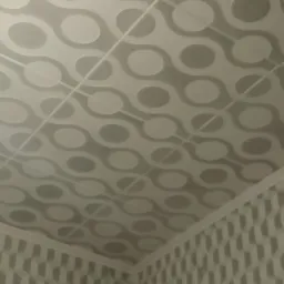 Szare płytki na suficie z wzorem kół połączonych liniami, widoczne także płytki na ścianie z geometrycznym wzorem, ujęcie z dołu.