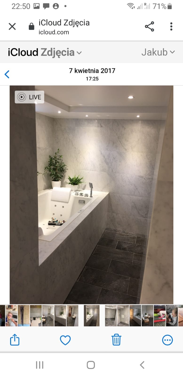 Elegancka łazienka z narożną wanną z hydromasażem, wykończona marmurowymi płytami na ścianach i ciemnoszarą podłogą, oświetlona punktowymi lampami w suficie, z roślinami doniczkowymi jako elementem...