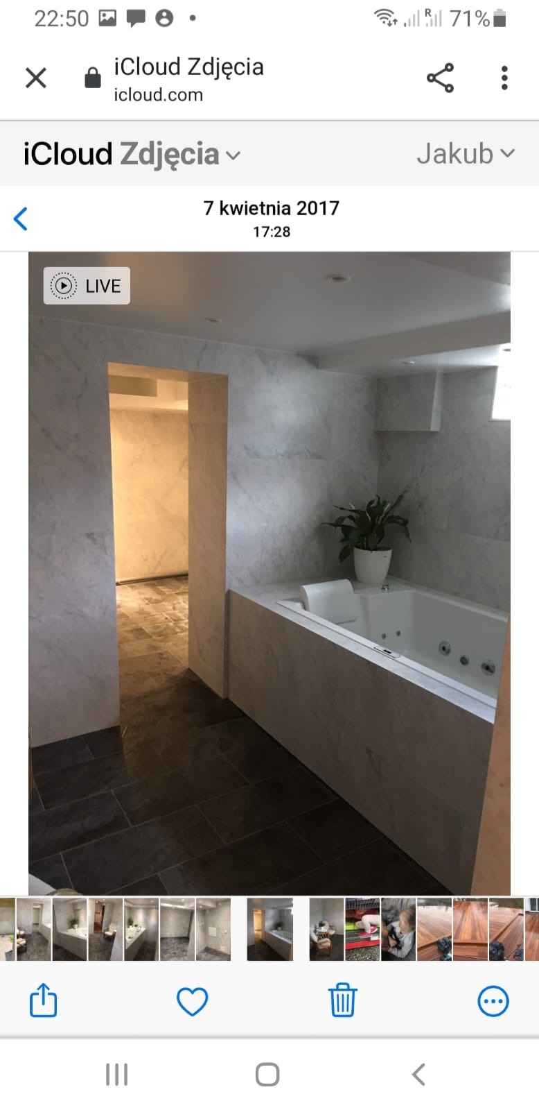 Wykończona łazienka z wanną z hydromasażem, marmurowymi płytkami ściennymi i ciemną podłogą z płytek, widok na sąsiednie pomieszczenie z surową podłogą.