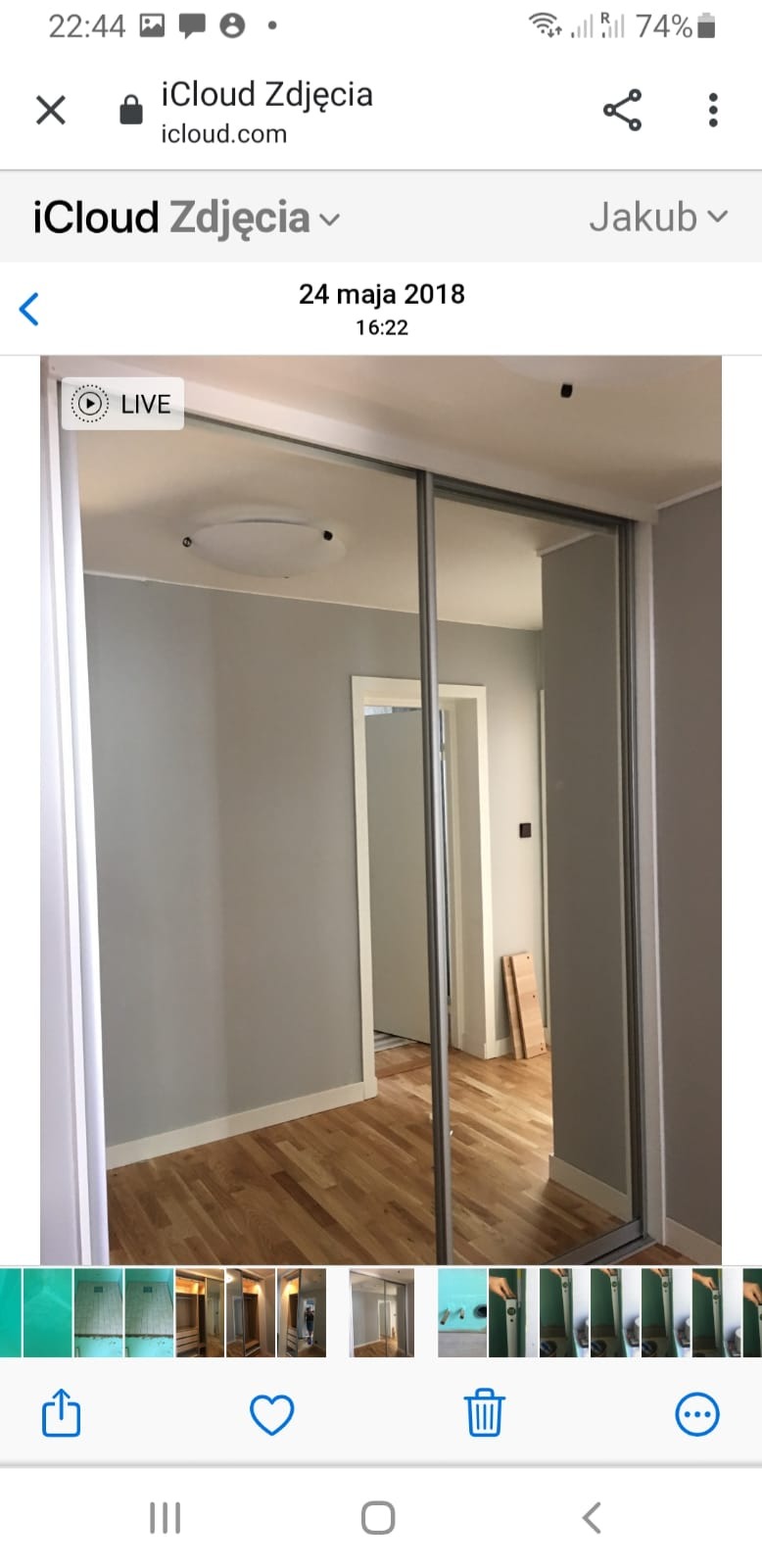 Wnętrze pokoju z przesuwną szafą z lustrzanymi drzwiami, widoczny drewniany parkiet, szare ściany z białymi listwami przypodłogowymi oraz drzwi do innego pomieszczenia w tle.