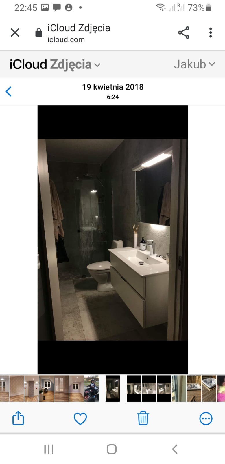 Nowoczesna łazienka z szarą, betonową ścianą, białą szafką pod umywalką z dwiema szufladami, toaletą i kabiną prysznicową ze szklanymi drzwiami.