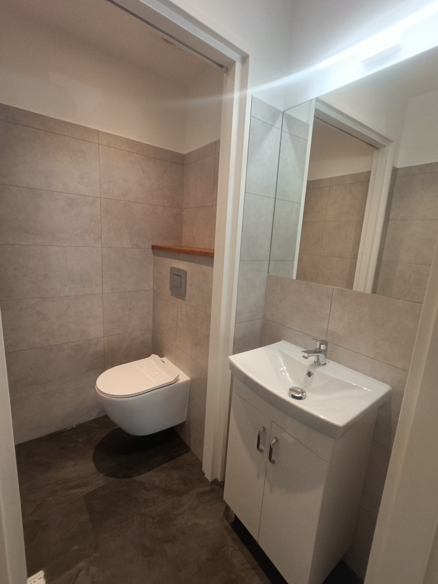 Nowoczesna łazienka w odcieniach szarości z podwieszaną toaletą, umywalką z szafką i płytkami imitującymi kamień na ścianach.