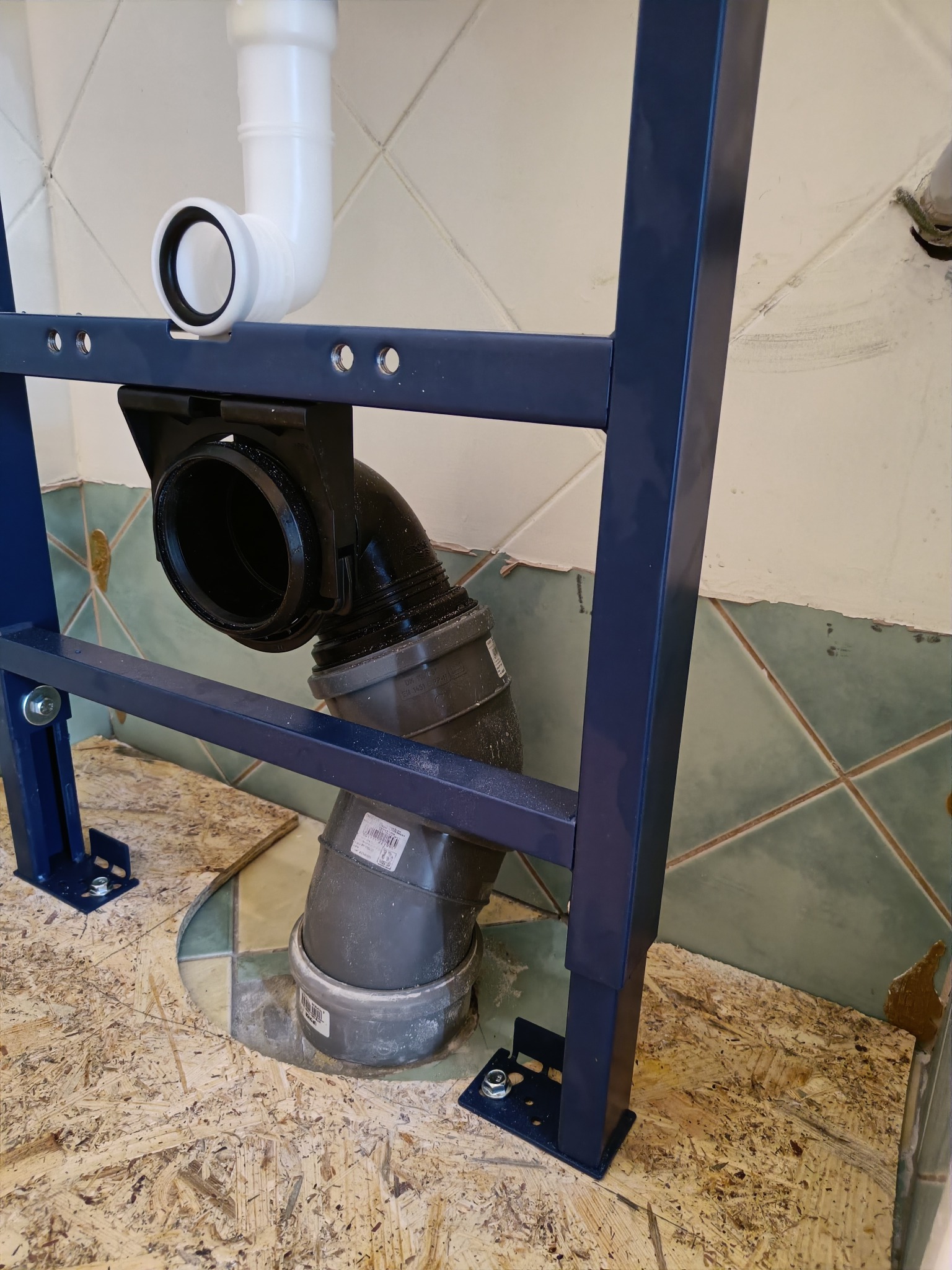 Stelaż podtynkowy WC z zamontowanymi rurami kanalizacyjnymi w trakcie instalacji w łazience z częściowo usuniętymi płytkami.