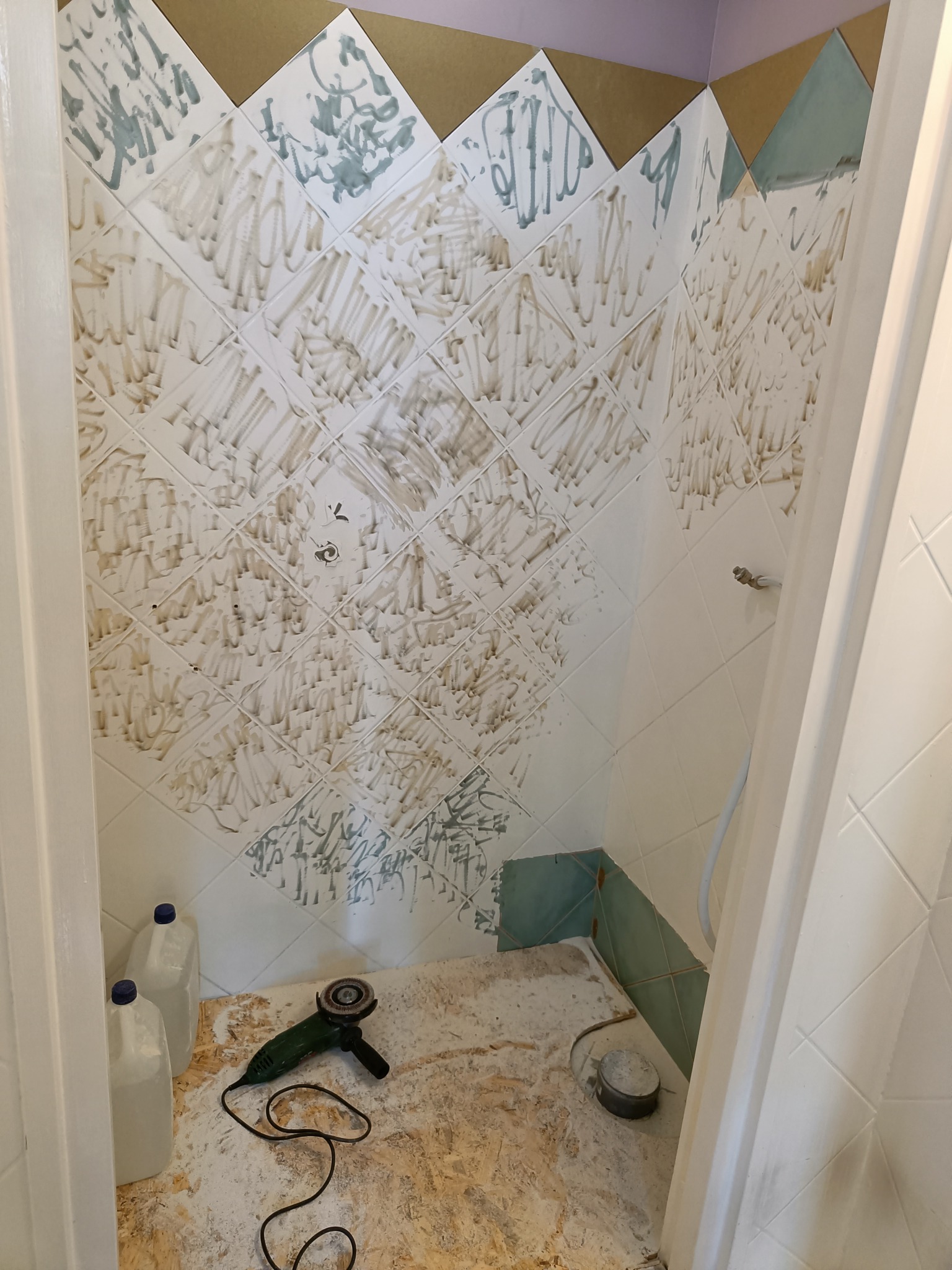 Przygotowanie ściany w łazience do położenia płytek, widoczne ślady po kleju, szlifierka kątowa na podłodze i butelki z płynem.