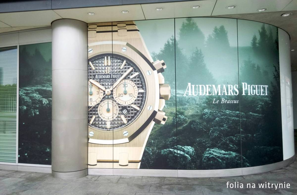 Reklama zegarka Audemars Piguet na witrynie sklepowej z motywem górskiego krajobrazu w tle.