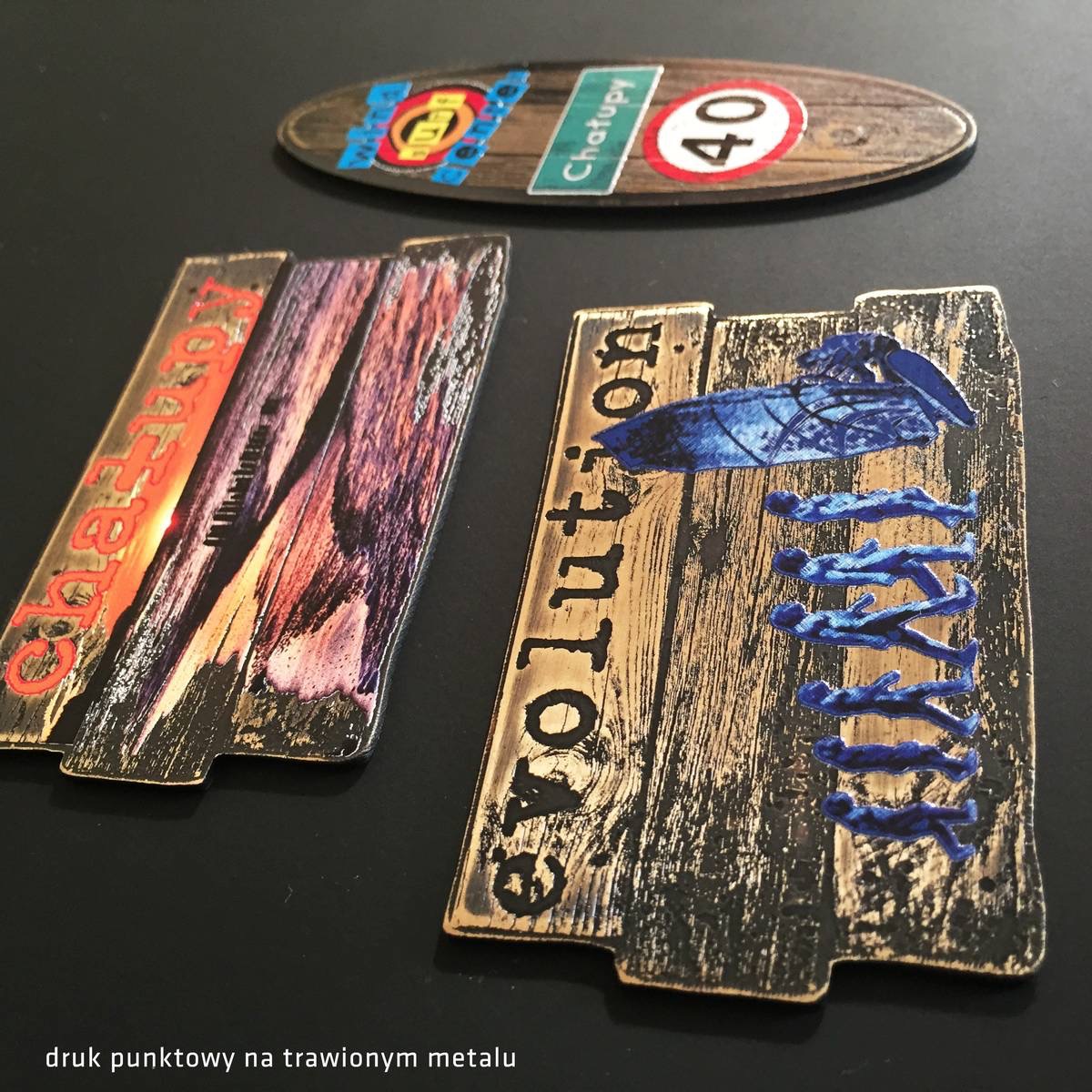 Metalowe naklejki z efektem trawienia, przedstawiające motywy podróżnicze i ewolucyjne, ułożone na czarnym tle.